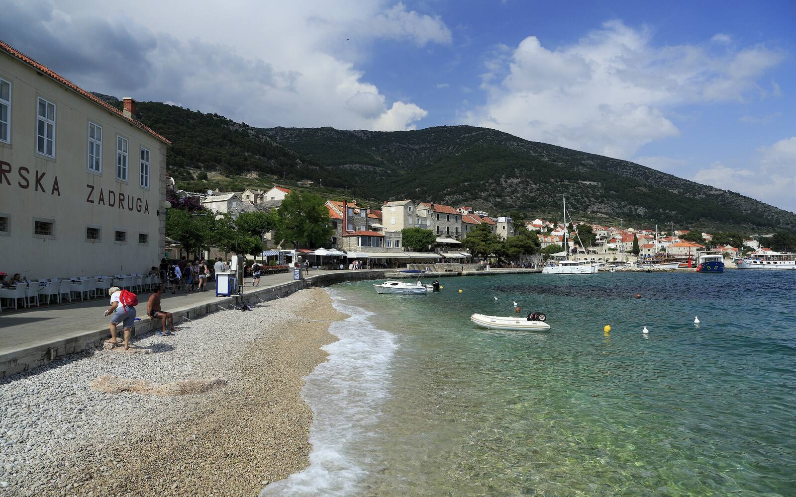 De waterkant van Bol op Brač met een kiezelstrand, helder water en de bergen erachter