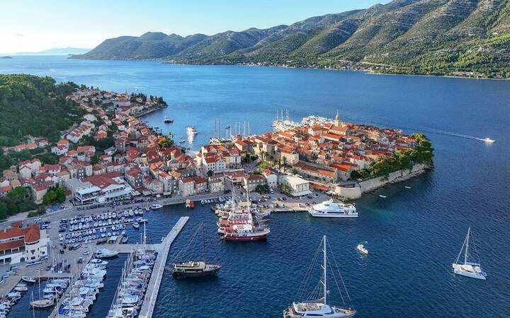 Luchtfoto van het ommuurde oude stadje van Korčula op een schiereilandje, met jachthaven en het Pelješackanaal