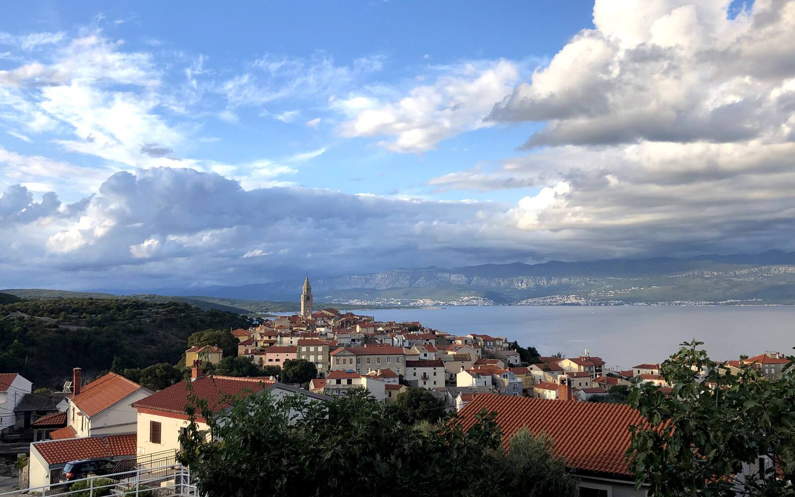 Uitzicht over de daken van Vrbnik op een klif boven zee, met de bergen van het vasteland op de achtergrond