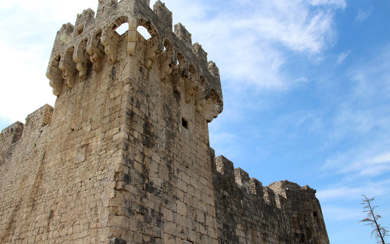De vierkante toren en kantelen van fort Kamerlengo in Trogir onder een blauwe lucht