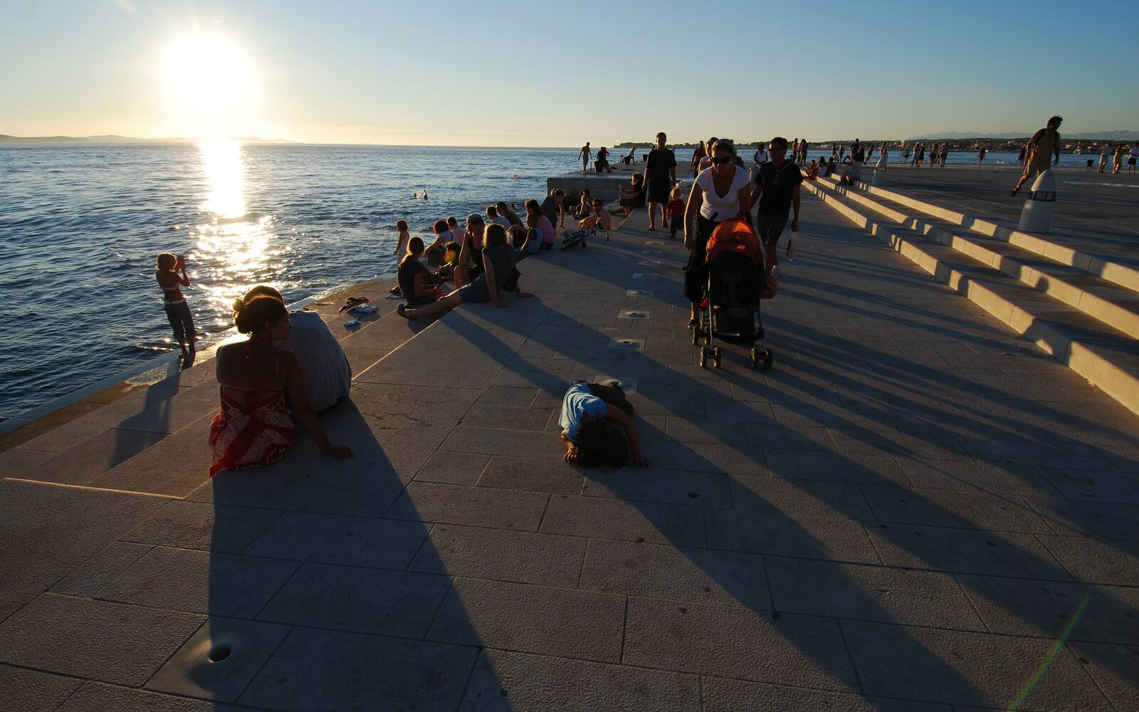 Mensen op de marmeren treden van het zeeorgel in Zadar bij zonsondergang boven zee