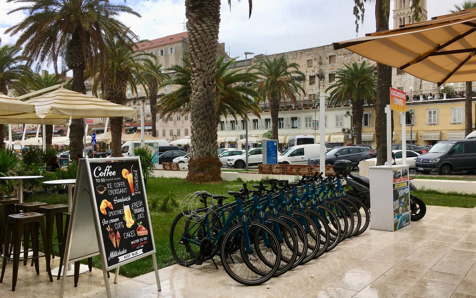 Terras met parasols, huurfietsen en palmbomen aan de Riva in Split, met historische gevels op de achtergrond