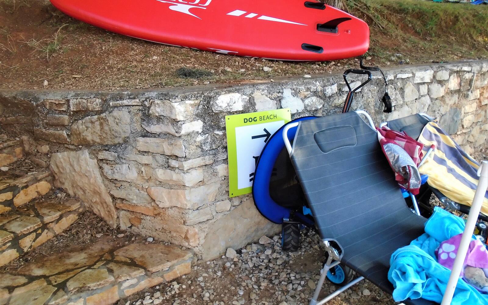 Bordje van een hondenstrand tussen strandstoelen en een supboard aan de rotskust bij Mareda in Istrië