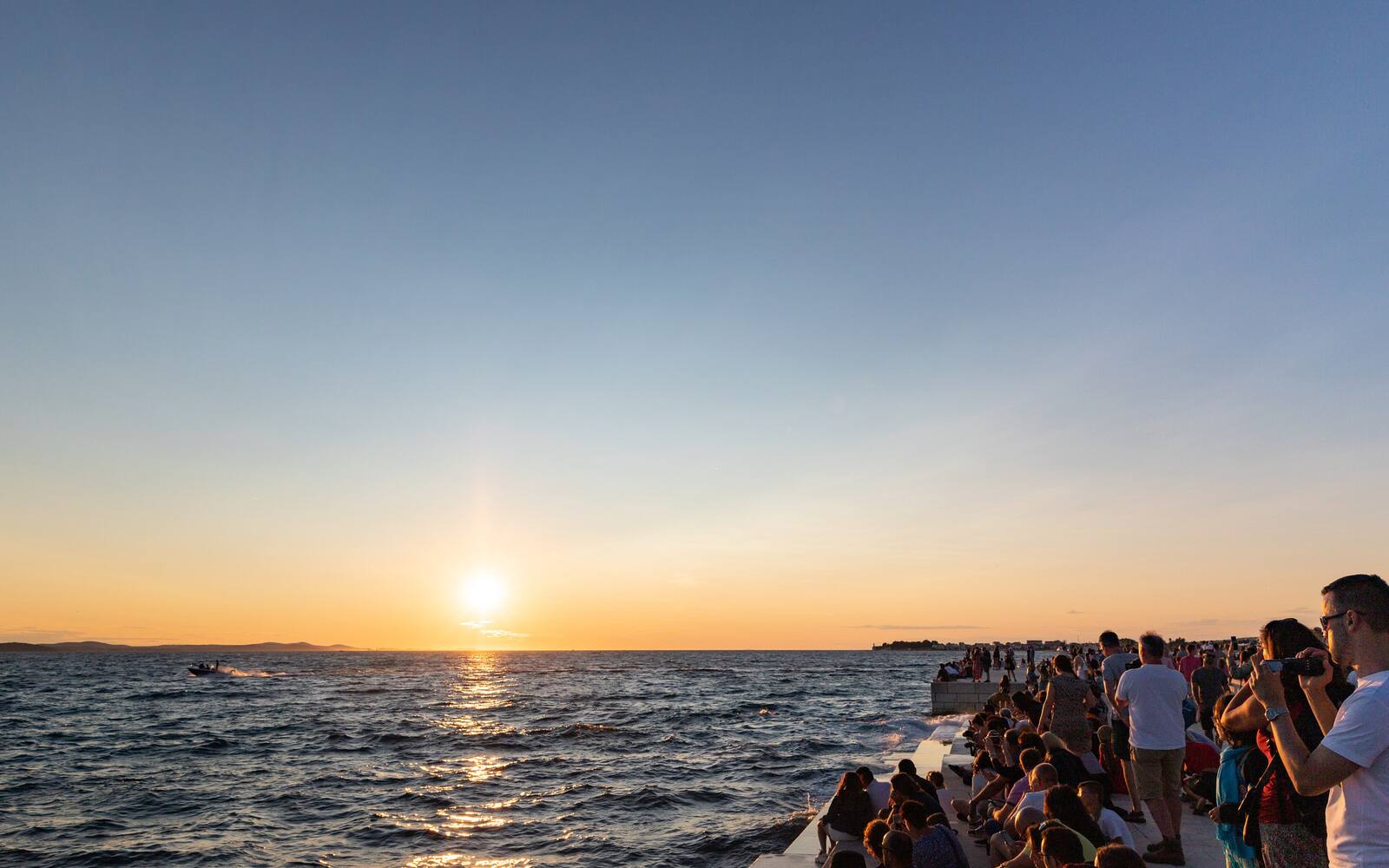 Zon die ondergaat boven de Adriatische Zee, gezien vanaf het Zeeorgel in Zadar met mensen op de treden