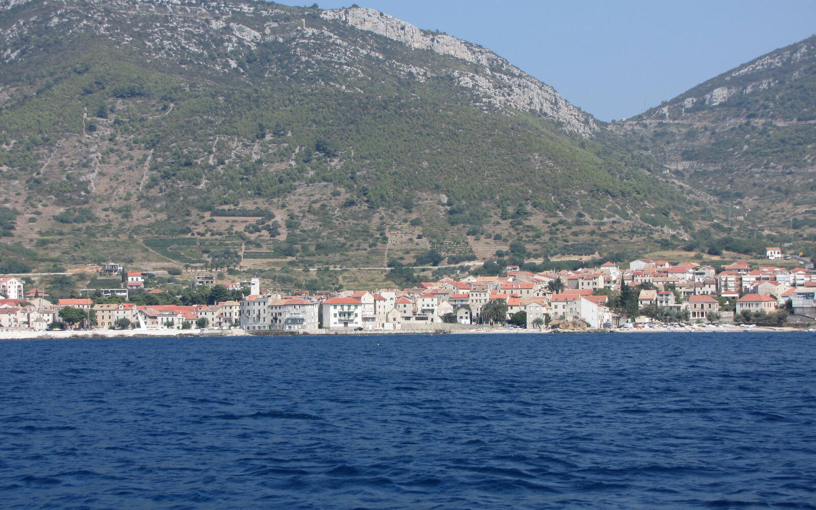 Het vissersdorp Komiža op Vis aan de voet van groene bergen, gezien vanaf de diepblauwe zee