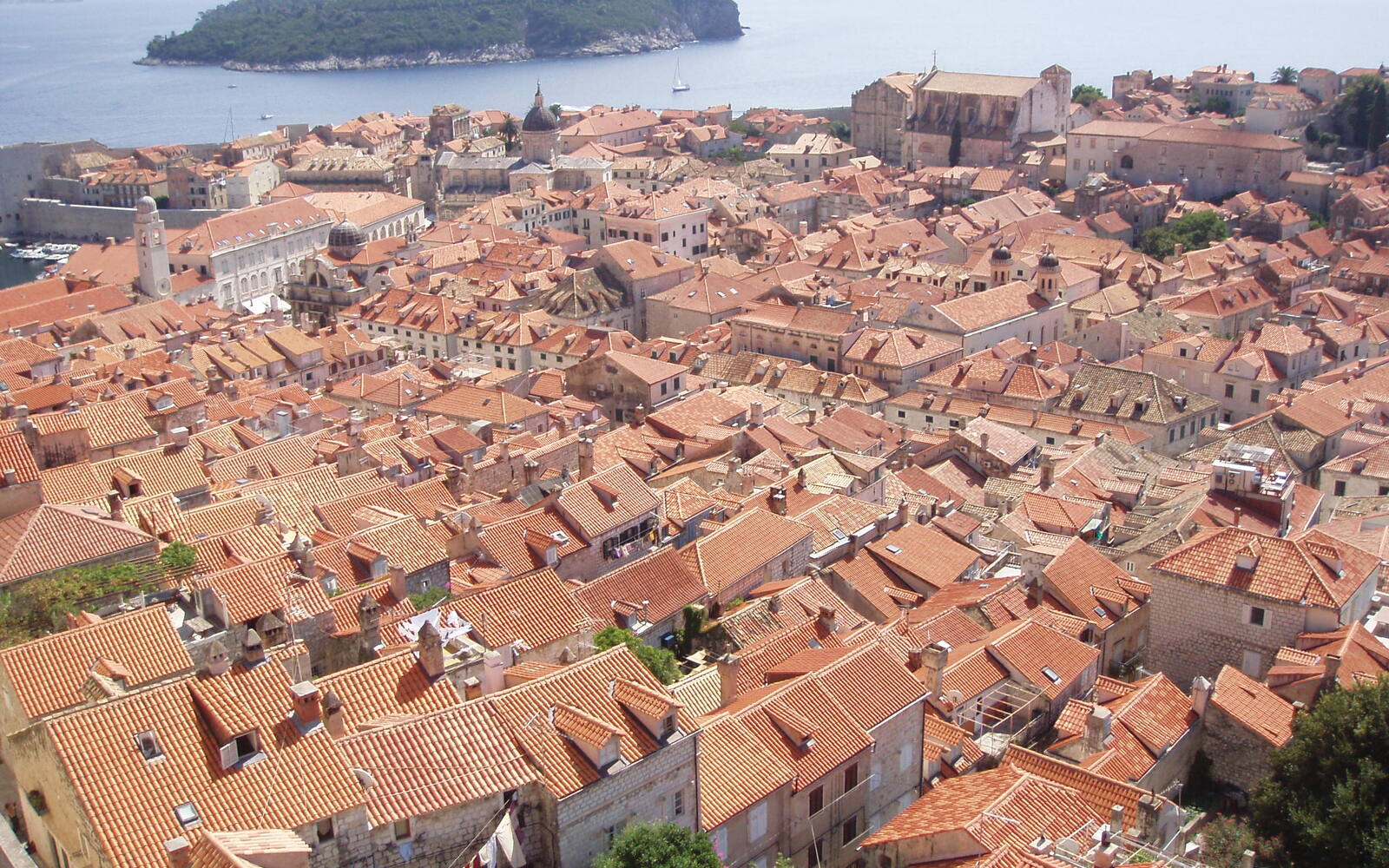 Uitzicht vanaf de stadsmuren over de oranje daken van de oude stad van Dubrovnik, met het eiland Lokrum in zee