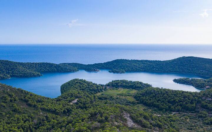 Luchtfoto van het zoutwatermeer Veliko jezero op Mljet, omringd door beboste heuvels met de zee op de achtergrond