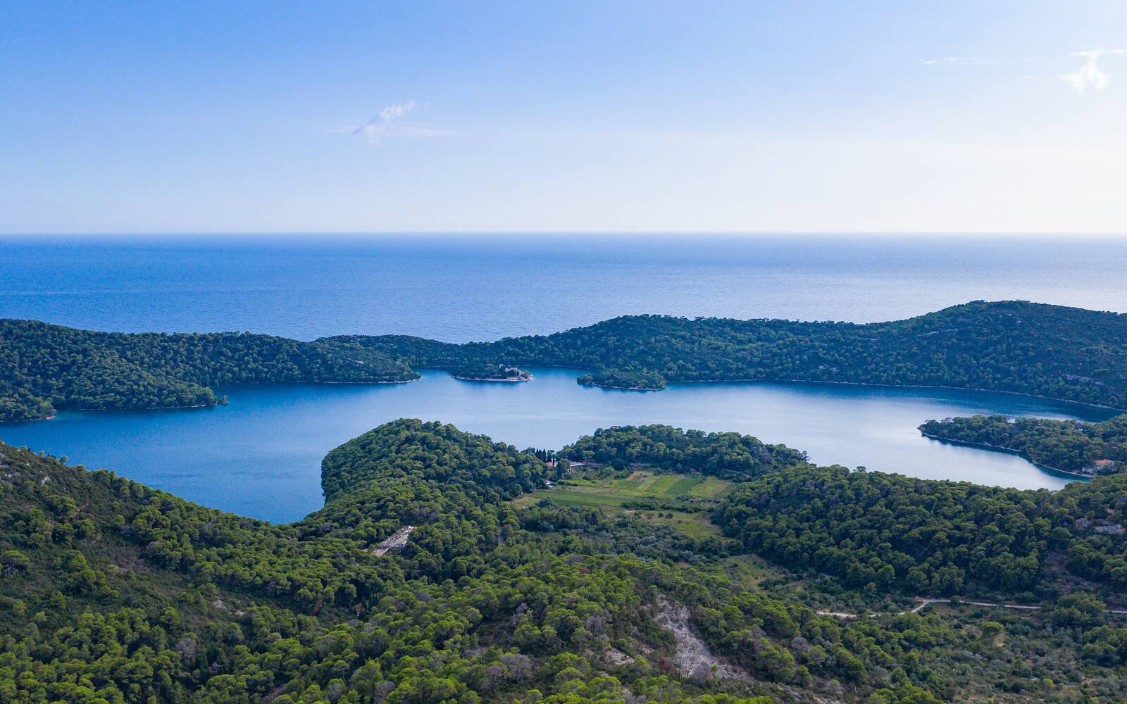 Luchtfoto van het zoutwatermeer Veliko jezero op Mljet, omringd door beboste heuvels met de zee op de achtergrond