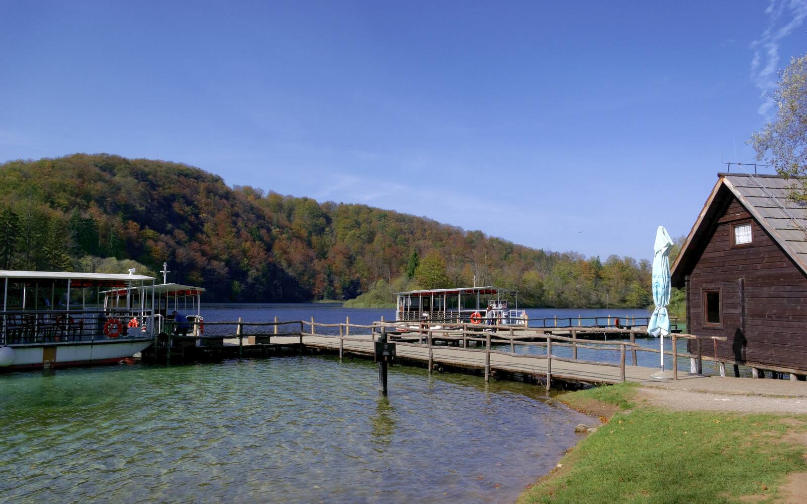 Houten steiger en boot aan een meer in de Plitvicemeren met herfstkleurige bossen