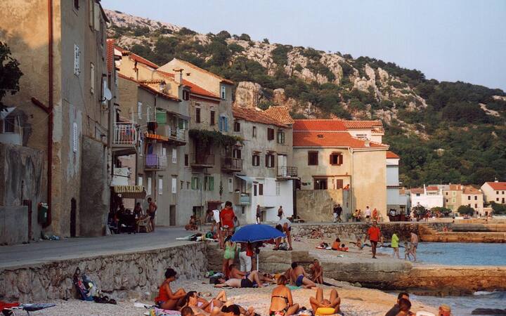 Kustdorp Baška op Krk met badgasten op de kiezels voor oude stenen huizen