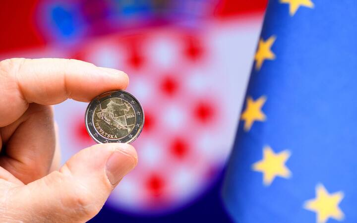 Hand houdt een Kroatische euromunt voor een vlag van Kroatië en de Europese Unie