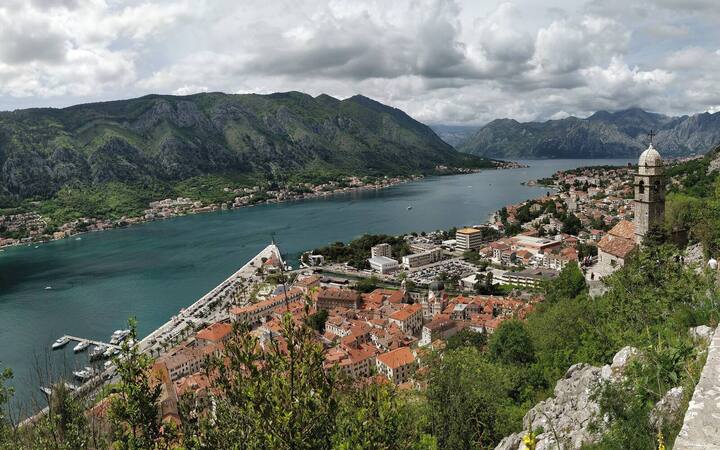 Uitzicht vanaf de stadsmuren over de baai van Kotor en de rode daken van de oude stad, met een cruiseschip in de haven