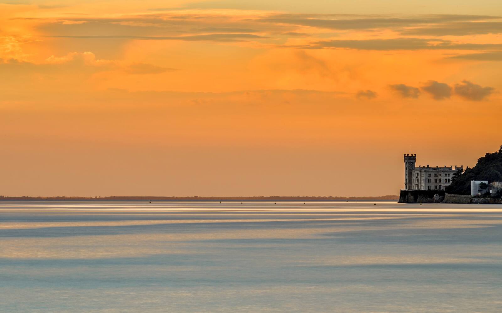 Kasteel Miramare op een rotspunt aan de Golf van Triëst bij een oranje zonsondergang